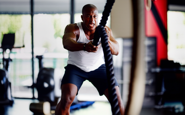 Athlete performing battle ropes during an intense high-intensity interval training session in a modern gym, showcasing full-body engagement and dynamic movement.